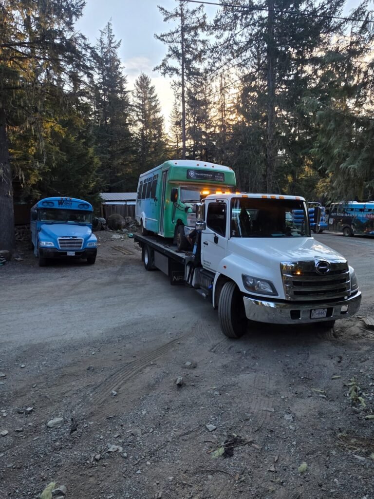 White tow truck transporting a green bus in a vehicle yard