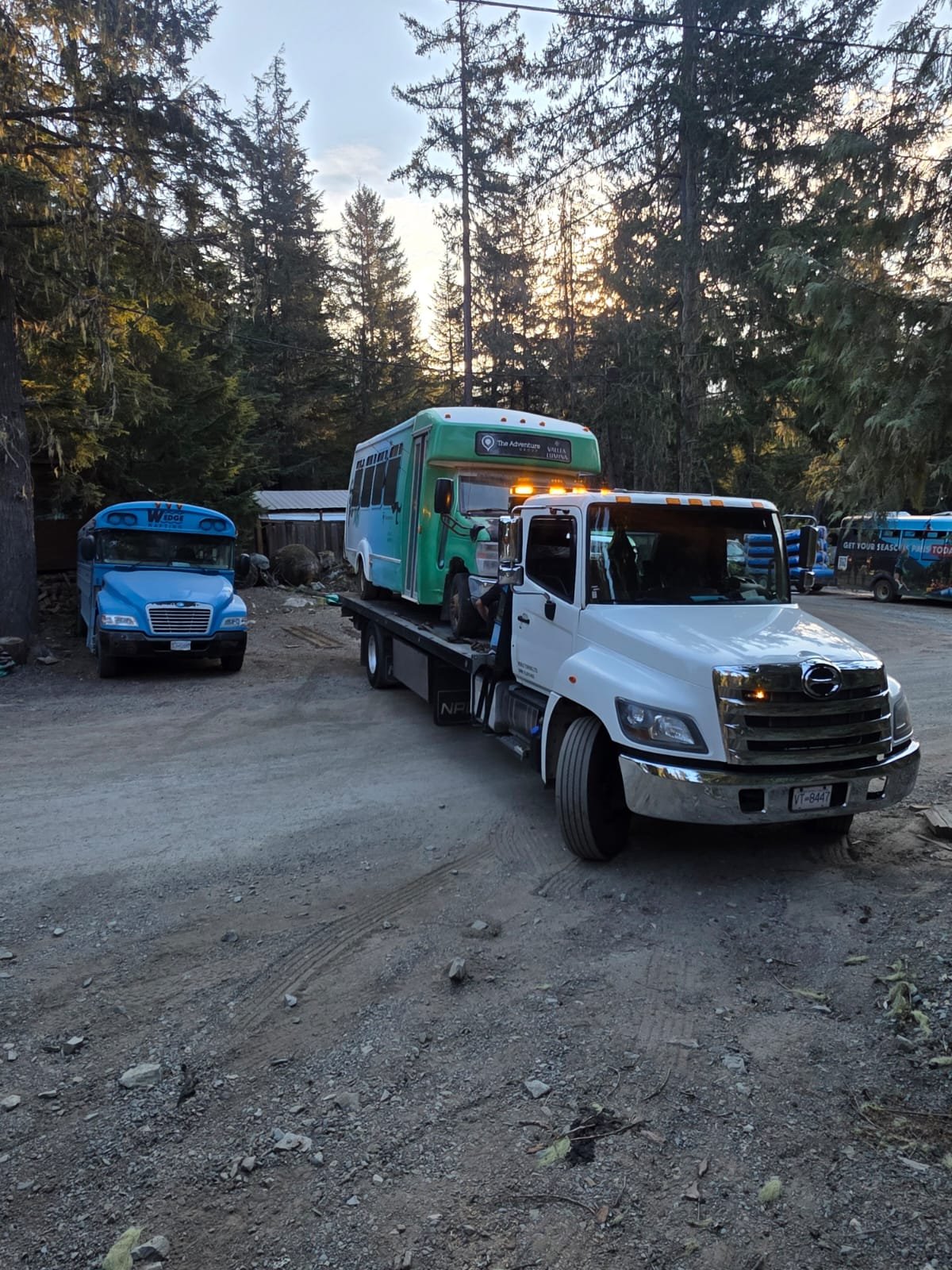 White tow truck transporting a green bus in a vehicle yard